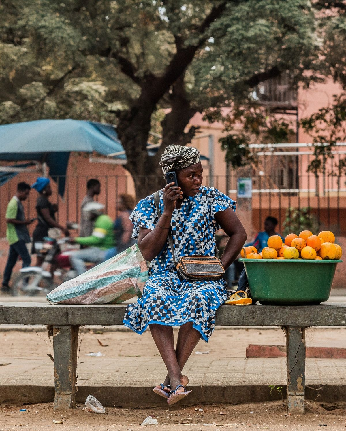 A woman speaking on her phone beside a basin of oranges at a roadside stall